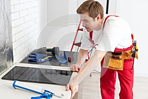 Young Repairman Installing Induction Cooker In Kitchen.