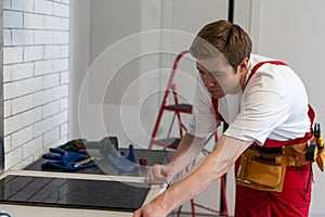 Young Repairman Installing Induction Cooker In Kitchen.