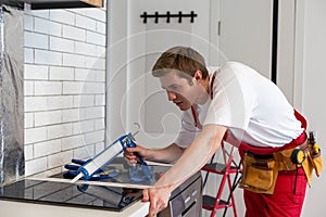 Young Repairman Installing Induction Cooker In Kitchen.