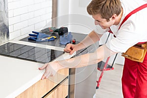 Young Repairman Installing Induction Cooker In Kitchen.