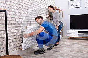 Repairman Installing Radiator On Brick Wall At Home