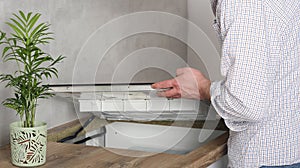 A young repairman installs a black induction hob in a modern white Scandinavian style kitchen