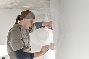 Young repairman smear on wall glue with a brush. Worker glueing wallpapers on concrete wall. Repair the apartment. Home