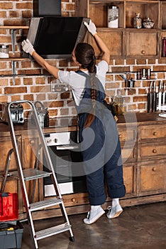 young repairwoman in overall examining stove hood