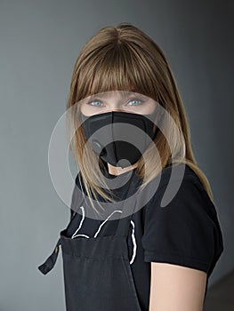 Young responsible blonde barber woman in barber`s apron wearing medical face mask for prevention infection spread of corona virus