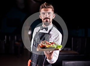 Young restaurant employee serves salad on a black background.
