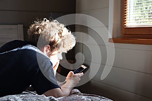 Young resting on bed holding cellphone, using smart device. Man using his mobile phone in his bedroom