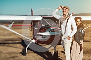 Young retro fashion couple posing in front of small plane