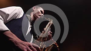 A young retro stylish guy plays on the golden shiny saxophone on stage. Dark studio with smoke and neon lighting. Bottom