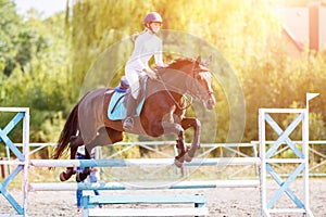 Young rider girl on bay horse jumping over barrier