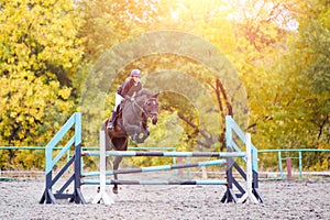 Young rider girl on bay horse jumping over barrier