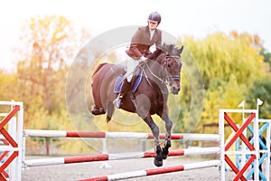 Young rider girl on bay horse jumping over barrier