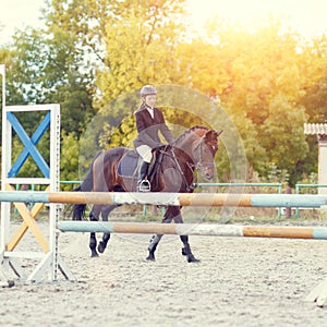 Young rider girl on horse striding along a hurdle