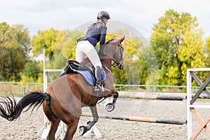 Young rider girl jumping over barier on her course