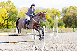 Young rider girl jumping over oxer on show jumping