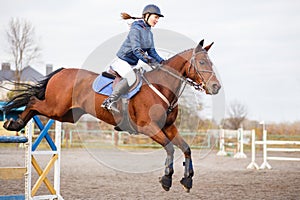 Young rider girl at show jumping. Jump hurdle