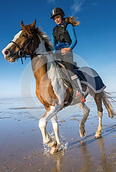 Young rider girl trotting on the beach with her mare