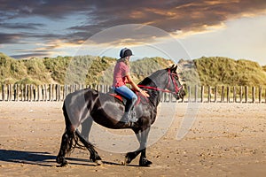 Beautiful young girl riding a Friesian mare on the coast of Hauts-de-France photo