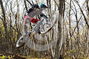 A young rider at the wheel of his mountain bike makes a trick in jumping on the springboard of the downhill mountain