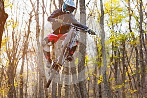 A young rider at the wheel of his mountain bike makes a trick in jumping on the springboard of the downhill mountain