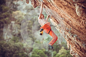 Young rock climber after jumping and gripping small handholds on overhanging cliff