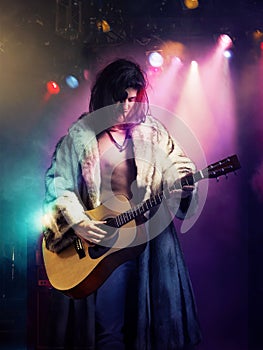 Young rock musician in fur coat playing guitar at concert