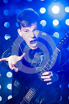 Young rock musician playing electric guitar and and making rock gesture. Rock star on background of spotlights