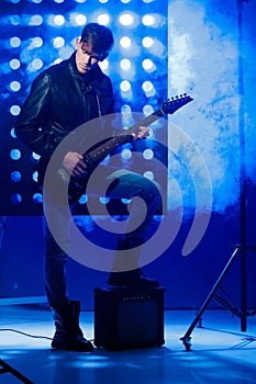 Young rock musician playing electric guitar and singing. Rock star on background of spotlights