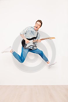 Young rocker playing on electro guitar, showing tongue and jumping
