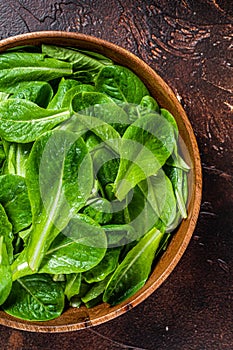 Young romain green salad leaves in wooden plate. Dark background. Top view