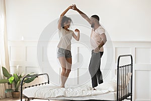 Young romantic african american couple wearing pajamas dancing on bed