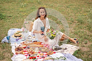 Young romantic brunette woman enjoy outdoor picnic on green lawn and hold glass of white wine