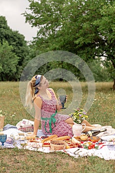 Young romantic brunette woman enjoy outdoor picnic on green lawn and hold glass of white wine