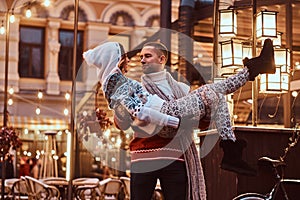 Young romantic couple enjoying spending time together at Christmas on street decorated with beautiful lights. Happy