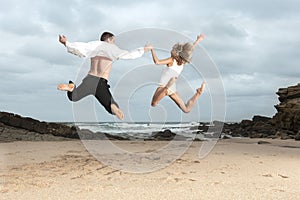 Young romantic couple jumping on the beach at sunrise