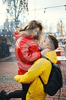 Young romantic couple in love hugging, wearning in bright yellow and red down jackets. Handsome man carrying young