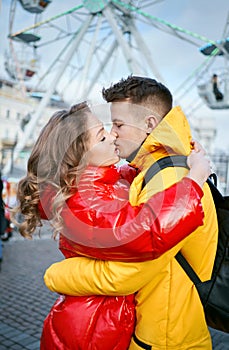 Young romantic couple in love kissing, hugging, walking on the street, wearning in bright down jackets. ferris wheel on