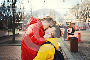 Young romantic couple in love kissing, hugging, wearning in bright yellow and red down jackets. Handsome man carrying