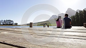 Young Romantic Couple Sitting On End Of Wooden Jetty By Lake