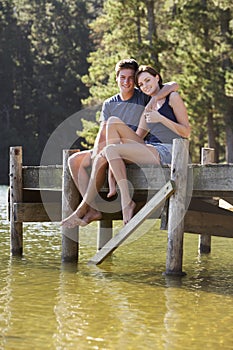 Young Romantic Couple Sitting On Wooden Jetty Looking Out Over Lake