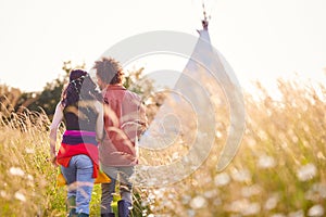 Young Romantic Couple Walking Through Field Towards Teepee On Summer Camping Vacation