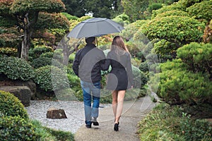 Young romantic couple walking together in park with umbrella