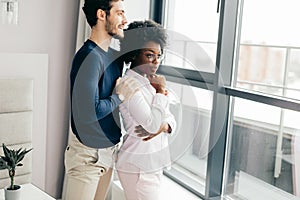 Romantic mixed race couple standing by the window thinking about their future.