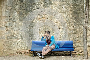 Young romantic man sitting alone on bench in front stone wall