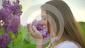 Young romantic smiling beautiful woman sniffing smelling lilac flowers in bouquet in nature outdoors