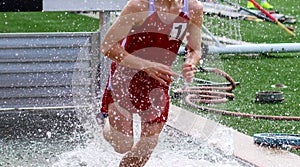 Young runner splashing in the water of the Steeplechase during a track race