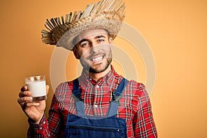 Young rural farmer man wearing countryside hat drinking organic milk from farm with a happy face standing and smiling with a