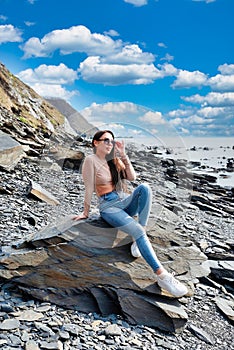 Young russian brunette woman in beige blouse sitting ont the stone near Japanese sea on a sunny day photo