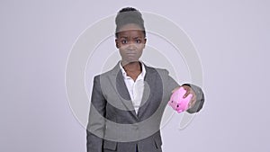 Young sad African businesswoman holding piggy bank and giving thumbs down