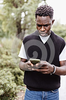 Young sad African man typing message, texting on phone outdoor